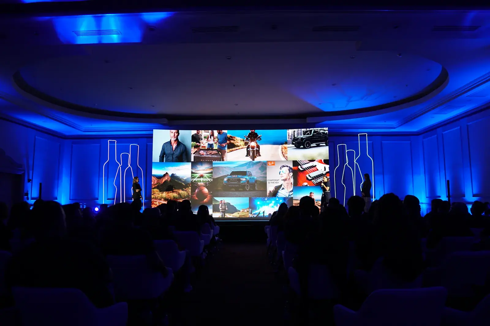 Plateia diante do telão de abertura, com as silhuetas das garrafas iluminadas em azul
