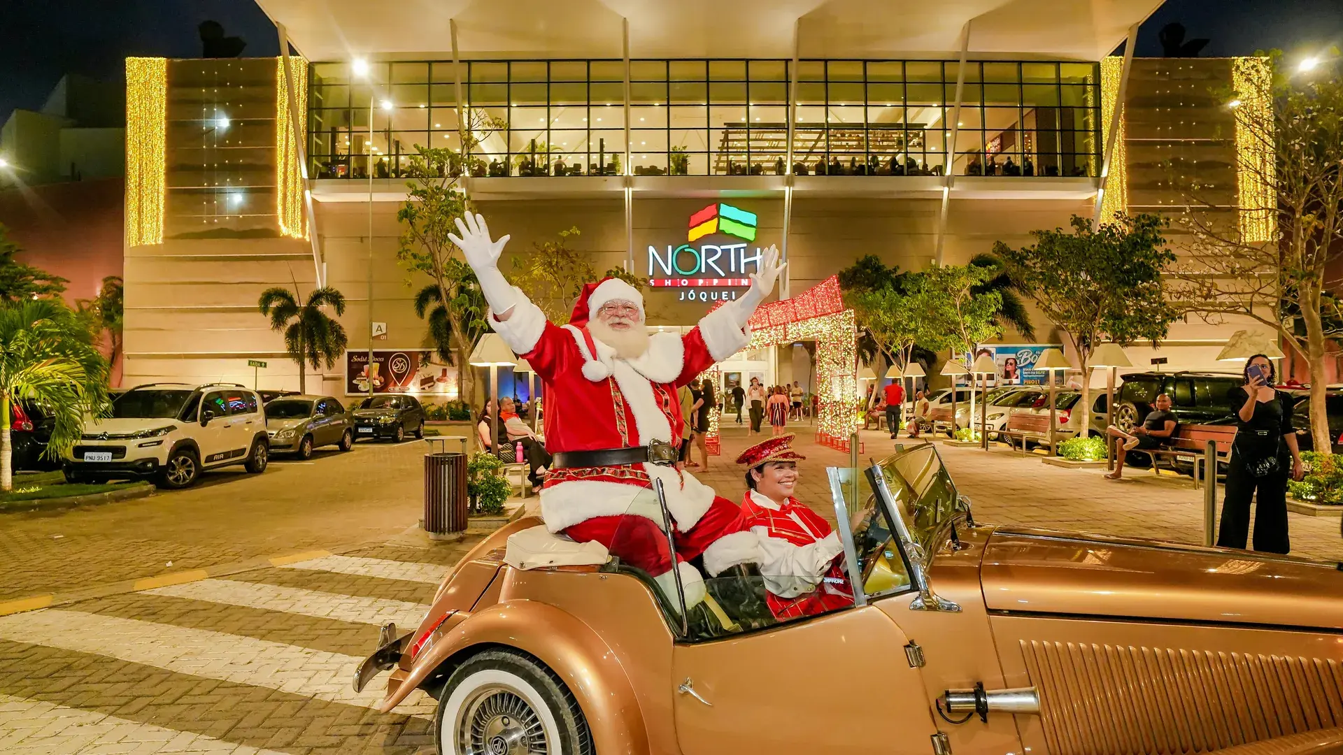 Santa waves from a vintage car at the mall entrance