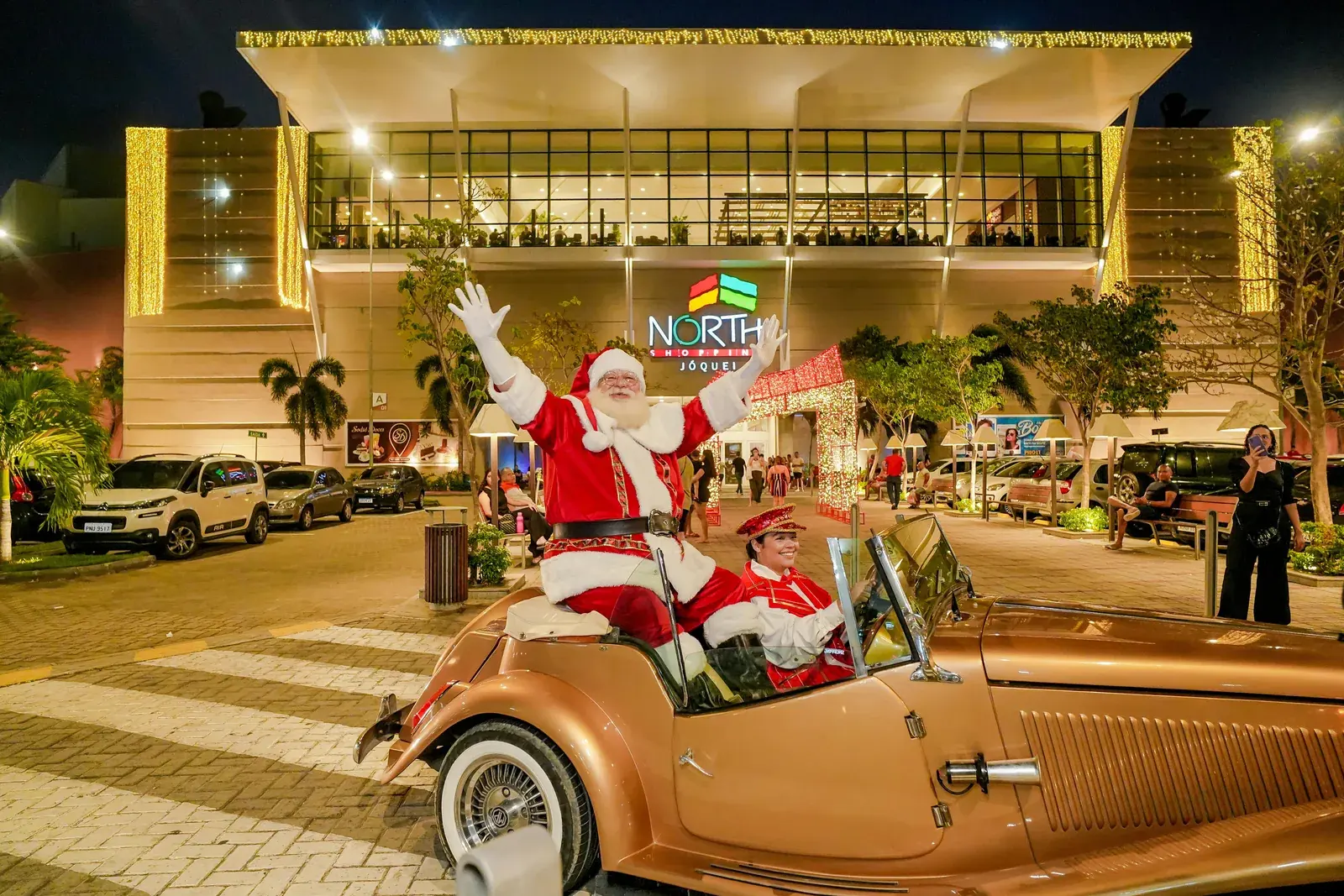 Santa waves from a vintage car at the mall entrance