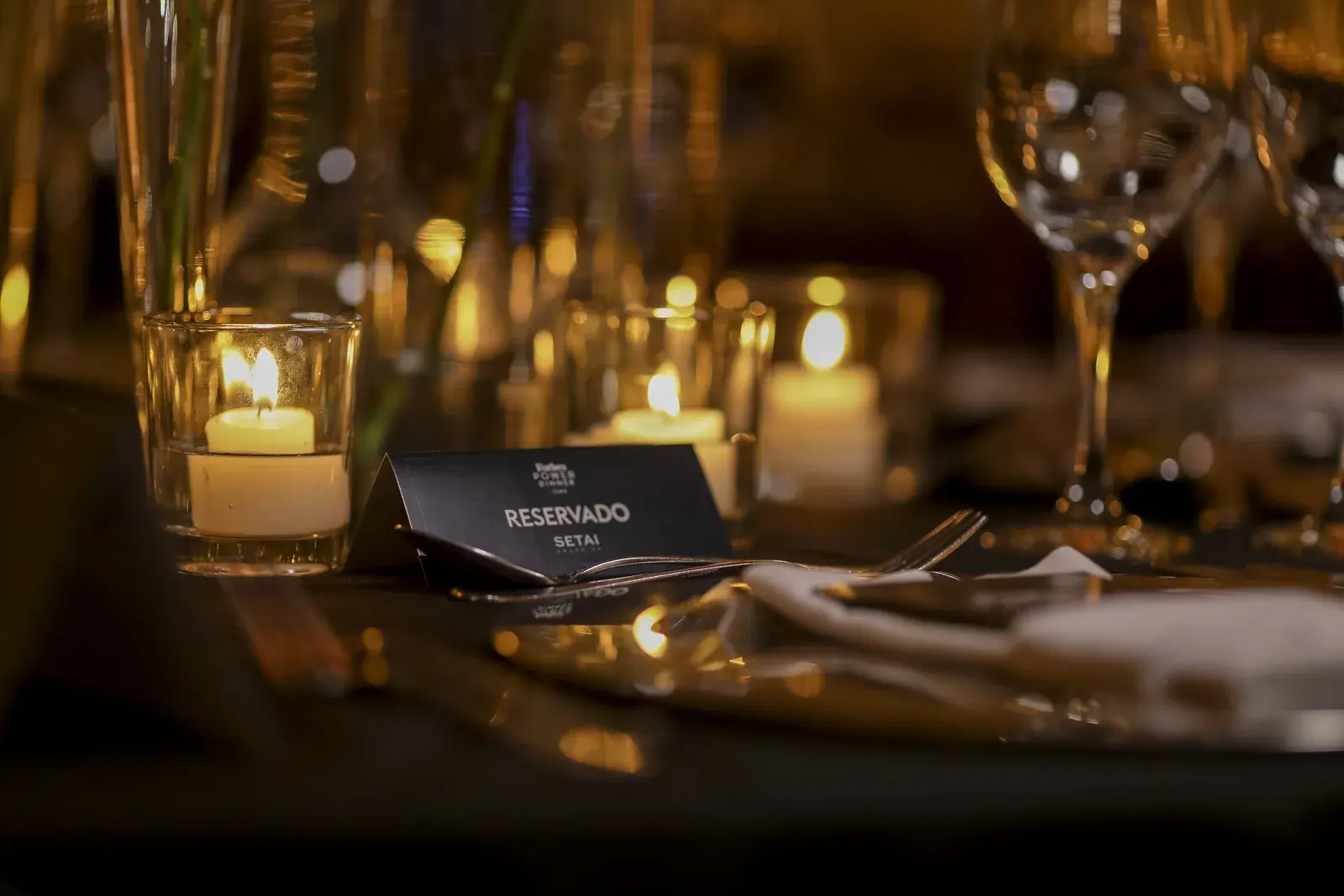 Detalhe da mesa posta, com velas, taças e o cartão de lugar reservado