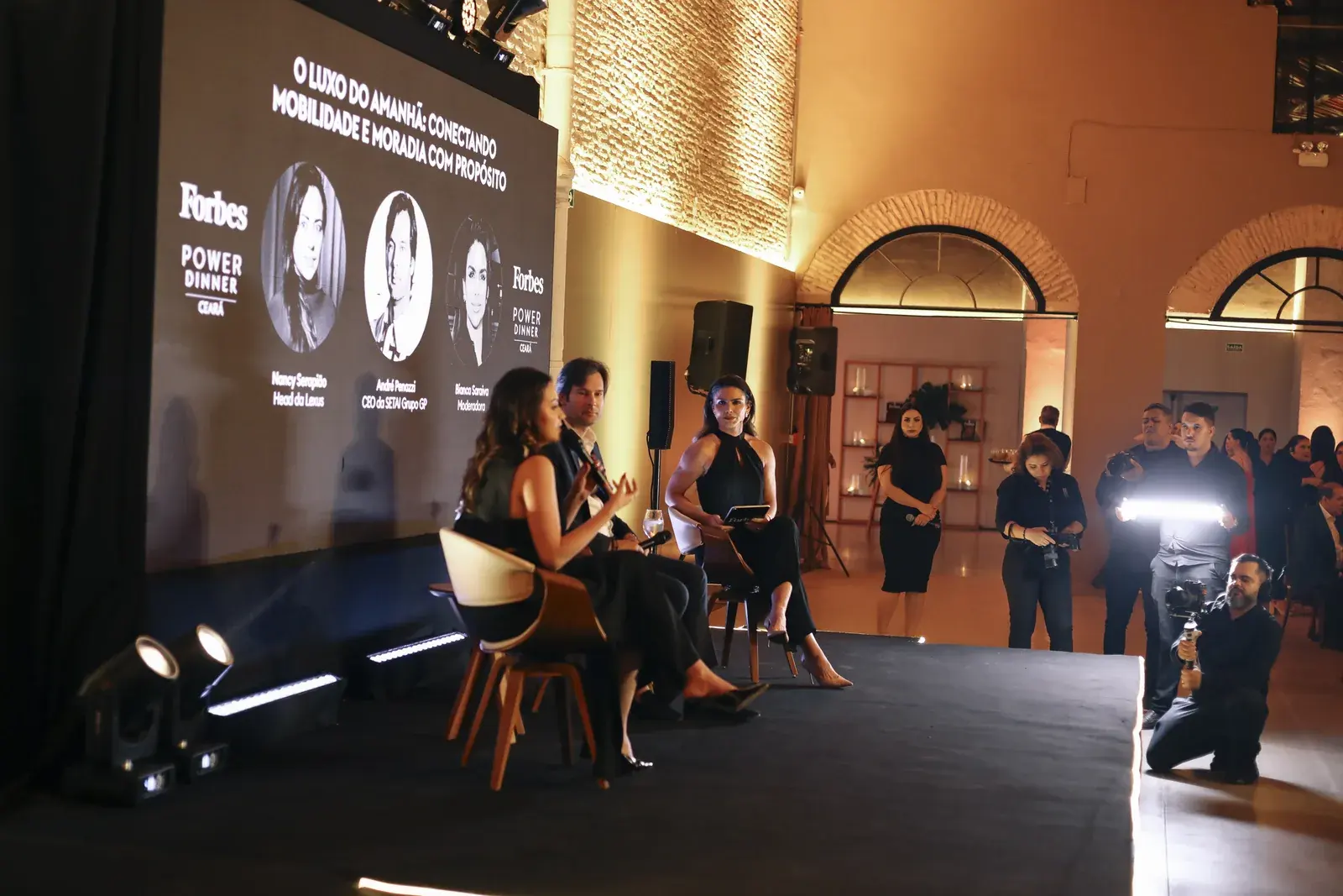 Painel de debate no palco diante do telão da Forbes