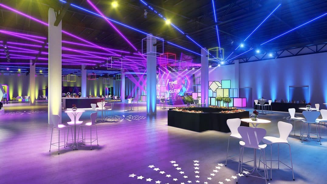 Salão do evento em luz azul e magenta, com lounges e pista