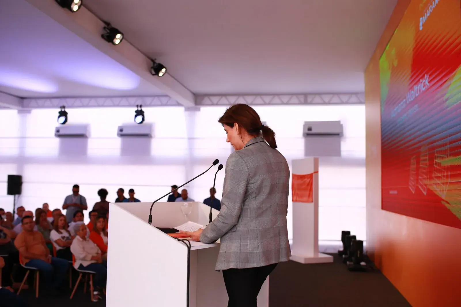 Executiva discursa no púlpito diante do painel do evento