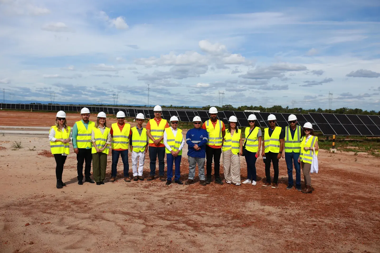 Equipe de colete e capacete posa diante das placas solares do complexo